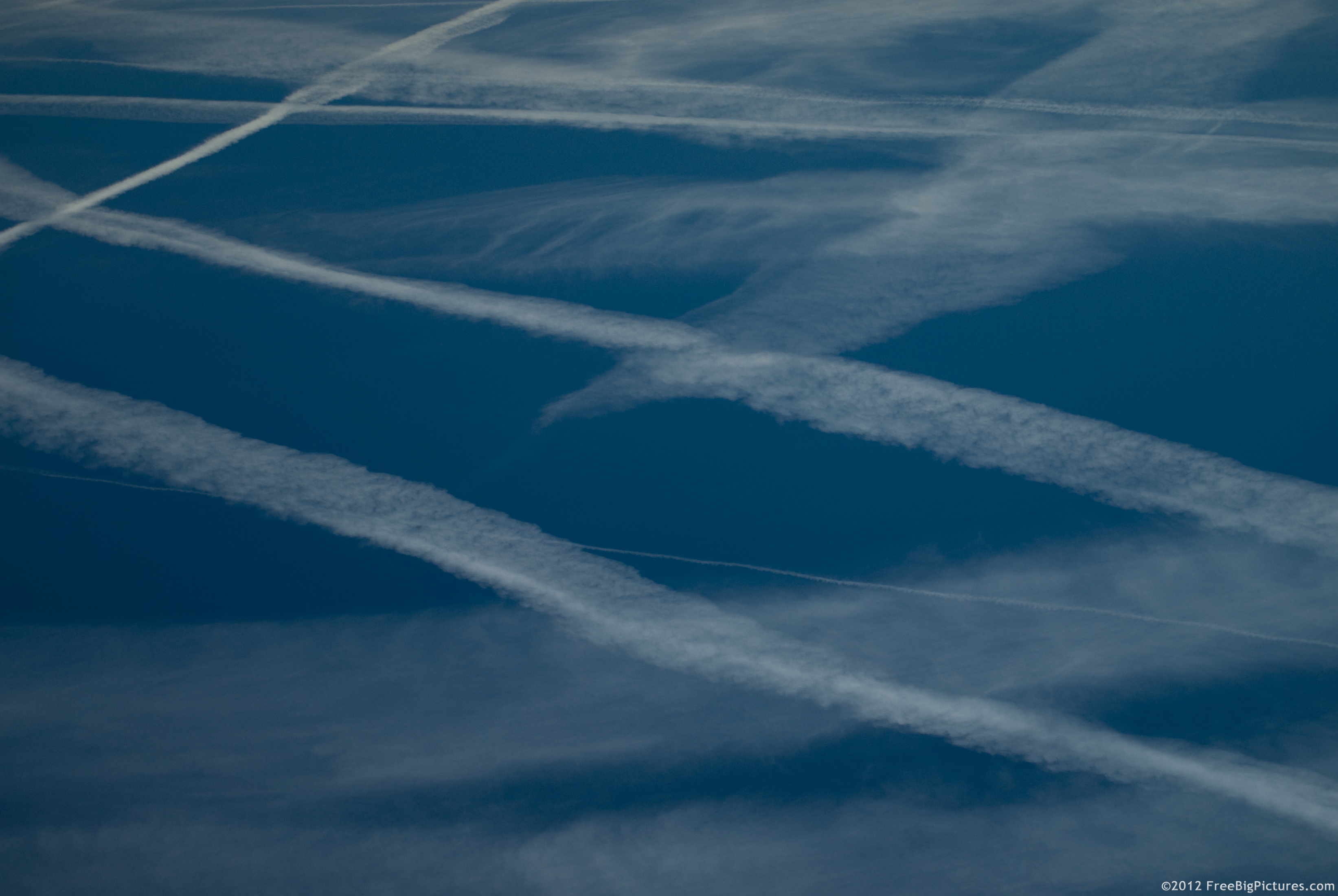 Lots of white traces on a blue sky left by the airplane engines composed mainly of carbon dioxide and water vapor. Maybe could be chemtrails according to the conspiracy theory followers.