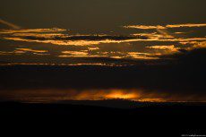 A sundown behind layers of clouds, in rusty shades